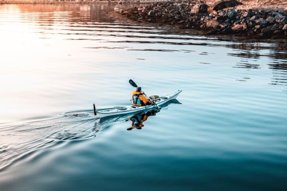 Kayaker paddles across calm waters near a rocky shoreline, perfect for a tranquil outdoor adventure.
