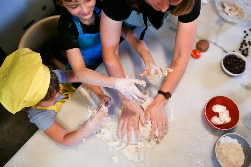 Kids and adult having fun baking cookies together in the kitchen, hands covered in flour.